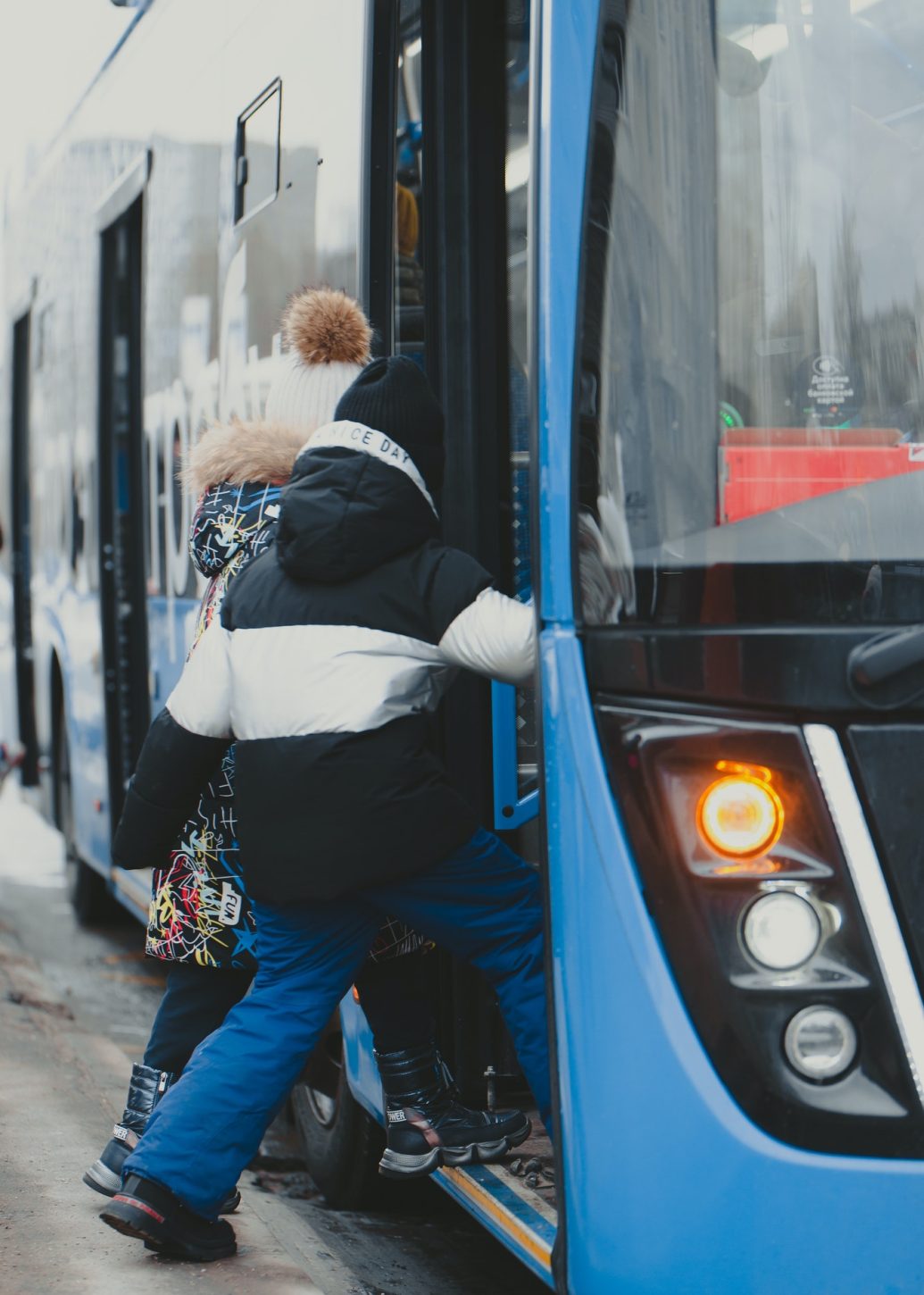 the-girls-enter-the-doors-of-a-blue-bus-that-has-arrived-at-the-bus-stop-.jpg